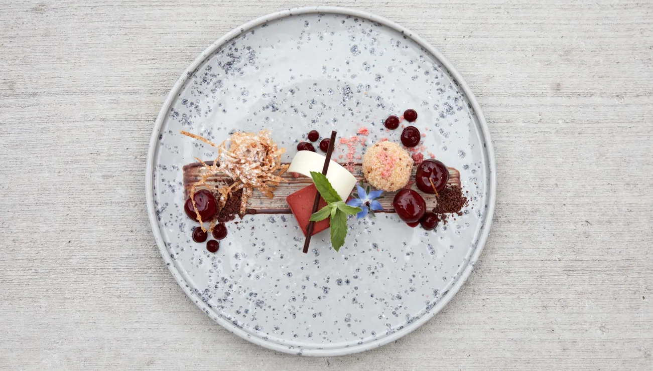 Gourmet-Dessert mit Schokolade, Beeren, Sahne und essbaren Blüten auf einem gesprenkelten Keramikteller