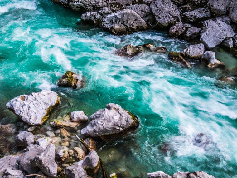 Fiume di montagna turchese limpido che scorre rapidamente tra le rocce