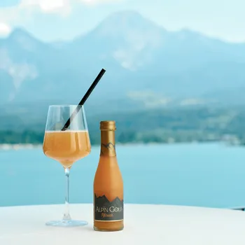 Peach drink in wine glass with Alpin Gold bottle on table by lake with mountain view